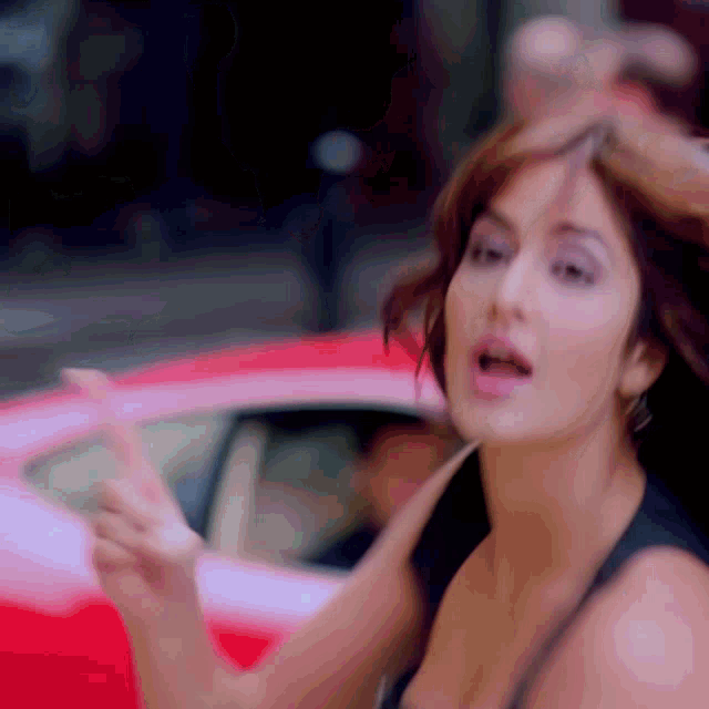 a woman is standing in front of a red car making a funny face