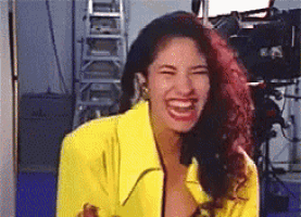 a woman in a yellow jacket is laughing in a room with a ladder in the background .