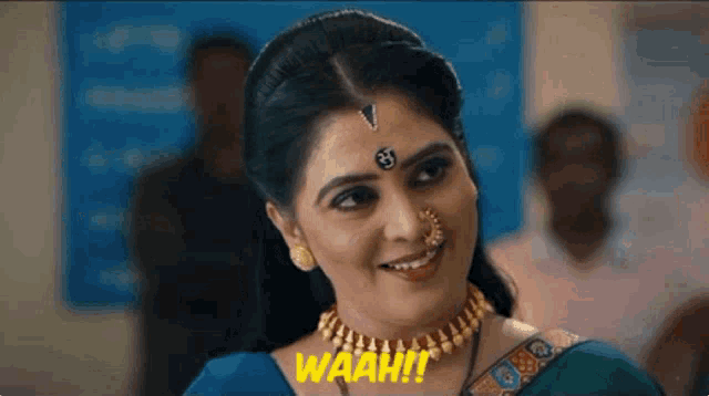 a woman wearing a nose ring and a necklace is smiling and says waah
