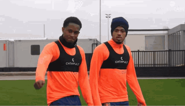 two soccer players wearing orange vests with the word catapult on them
