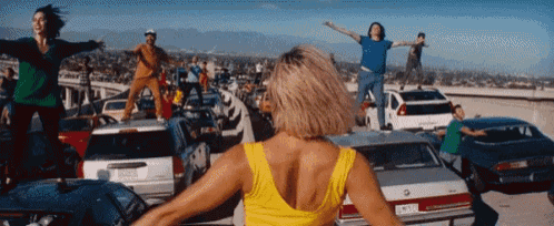 a woman in a yellow tank top is dancing in a parking lot