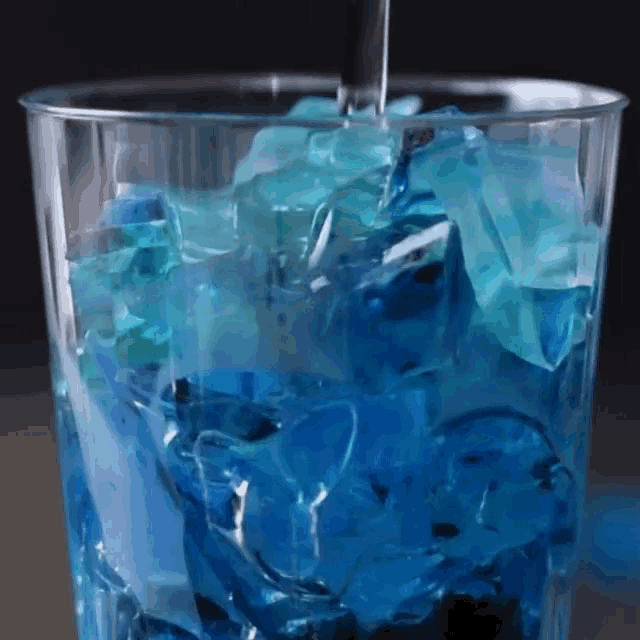 blue liquid is being poured into a glass filled with blue ice cubes