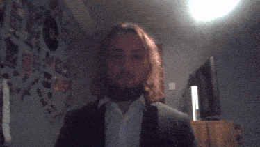 a man with long hair and a beard is standing in front of a wall with stickers on it including one that says bbc