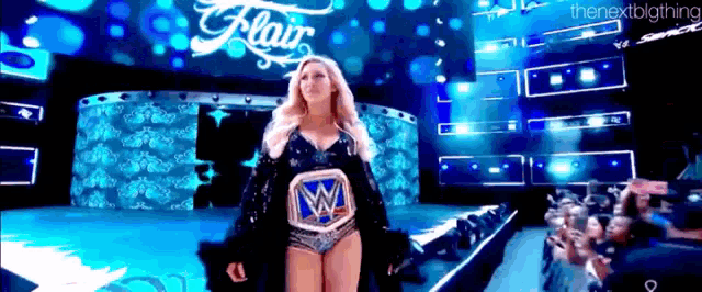 a woman is walking on a stage with a wrestling belt on her chest .
