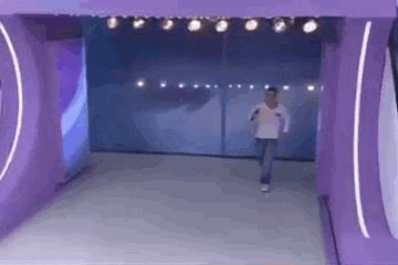 a man is walking through a purple tunnel with lights on .