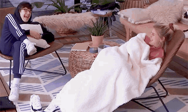 a woman is wrapped in a blanket while sitting in a chair next to a man .