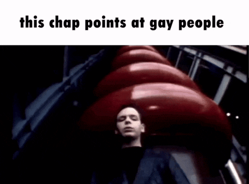 a man in a black shirt is standing in front of a large red balloon with the caption this chap points at gay people