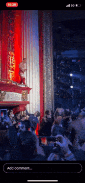 a phone screen shows a man standing on a stage with a crowd behind him and the time of 10:39