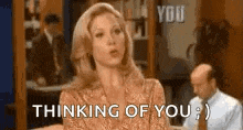 a woman is sitting on a couch and saying `` thinking of you '' in front of a man in a suit .