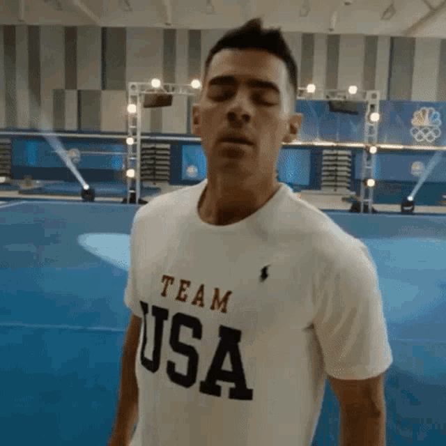 a man wearing a team usa t-shirt is standing in a gym with his eyes closed .