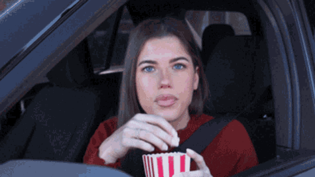 a woman in a car eating popcorn from a striped container