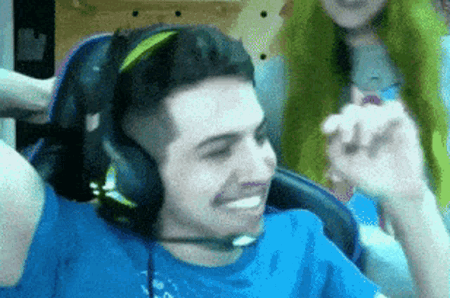 a man wearing headphones and a blue shirt is sitting in a chair with his arms outstretched .