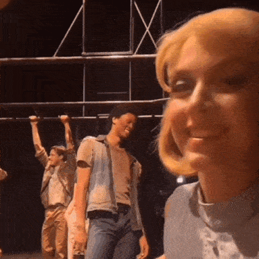 a woman with blonde hair is smiling in front of a group of men