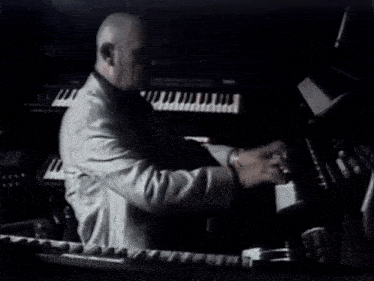 a man in a suit is playing a piano in the dark