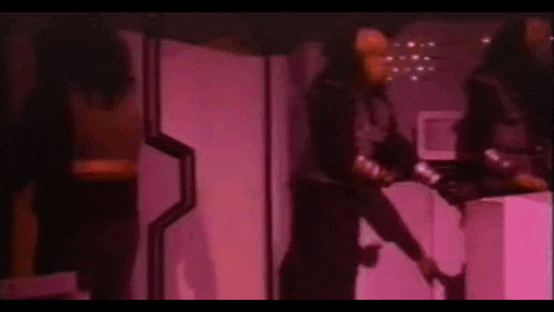 a man in a mask is standing in front of a pink wall in a room .
