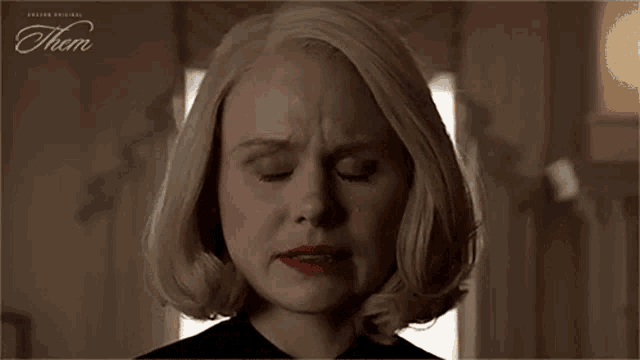 a woman with blonde hair and red nails is covering her face with her hand .