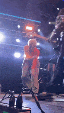 a man is playing a guitar on a stage while another man is standing behind him .