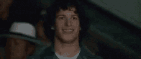 a man with curly hair is smiling in a blurry photo while wearing a hat .