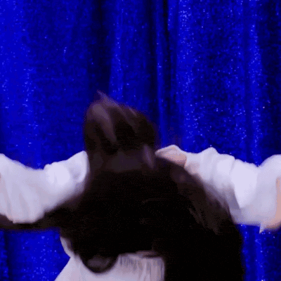 a woman in a white shirt is standing in front of a blue curtain with her arms outstretched .