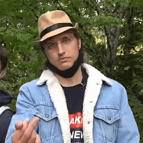 a man wearing a hat and a denim jacket is making a middle finger gesture .