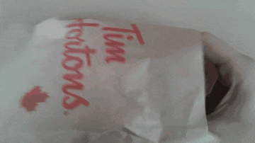 a person is holding a muffin next to a bag that says tim hortons