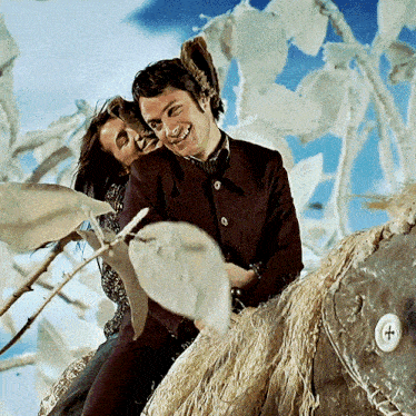a man and a woman are sitting on a sculpture and the man is wearing a purple jacket