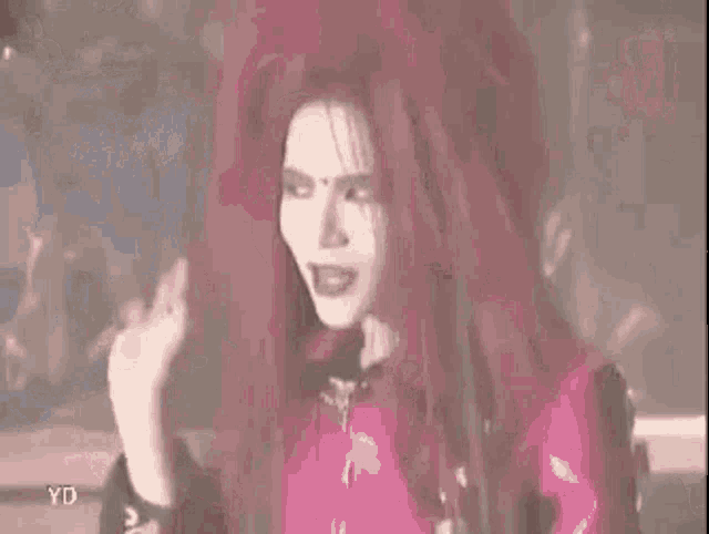 a woman with very long red hair is wearing a pink jacket and a black shirt .