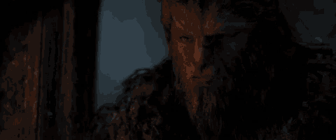 a close up of a man with a beard and horns in a dark room with a candle in the background .