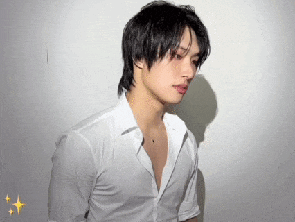 a young man in a white shirt and necklace is standing in front of a white wall .