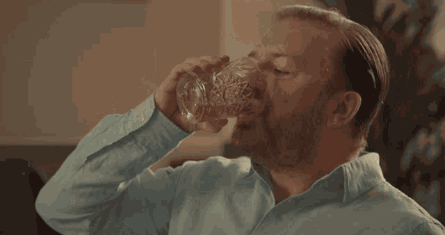 a man in a blue shirt is drinking a glass of water