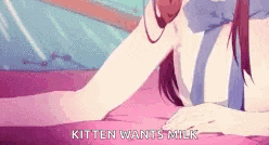 a girl is laying on a bed and talking on a phone while a kitten wants milk .