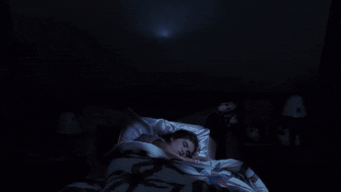 a woman is laying in bed with a ghost coming out of the ceiling above her .