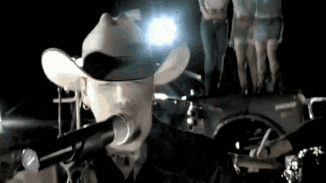 a man wearing a cowboy hat is singing into a microphone