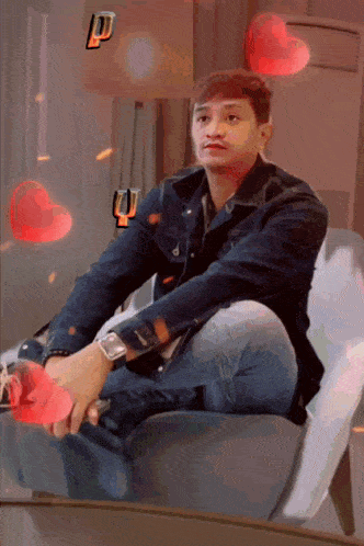 a man in a denim jacket sits in a chair surrounded by red hearts