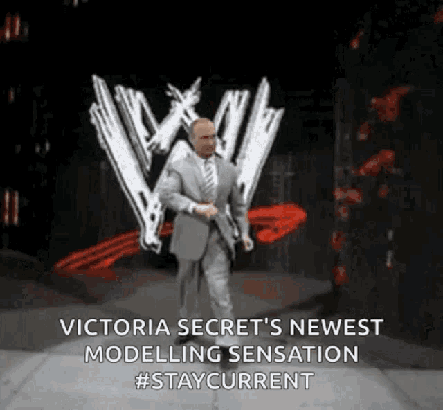 a man in a suit and tie is walking on a stage in front of a victoria secret sign .
