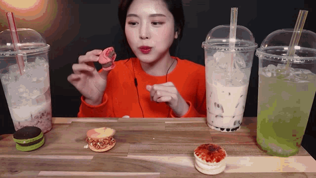a woman sitting at a table with three cups of drinks and a sandwich