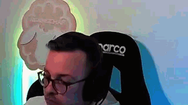 a man wearing glasses and headphones is sitting in a chair with a narco logo on it .