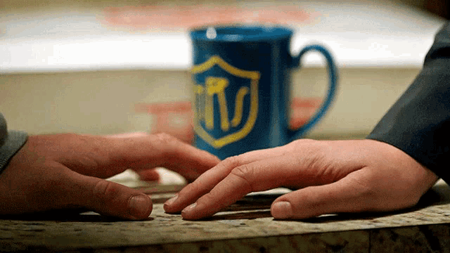 a person touching another person 's hand with a blue mug in the background