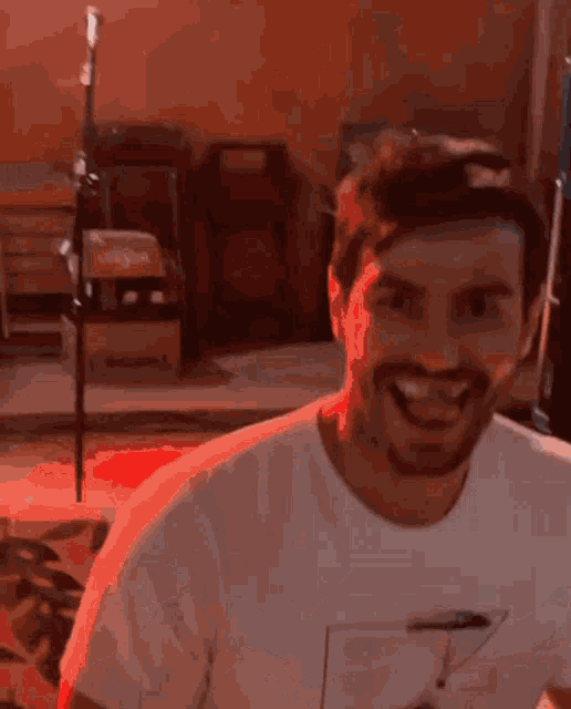 a man with a beard is smiling and wearing a white shirt with the word t on it