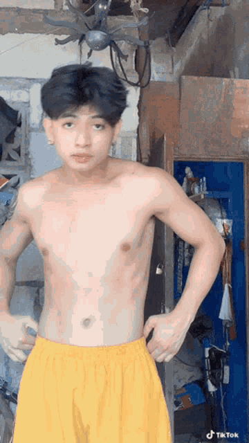 a shirtless young man in yellow shorts is standing in a room