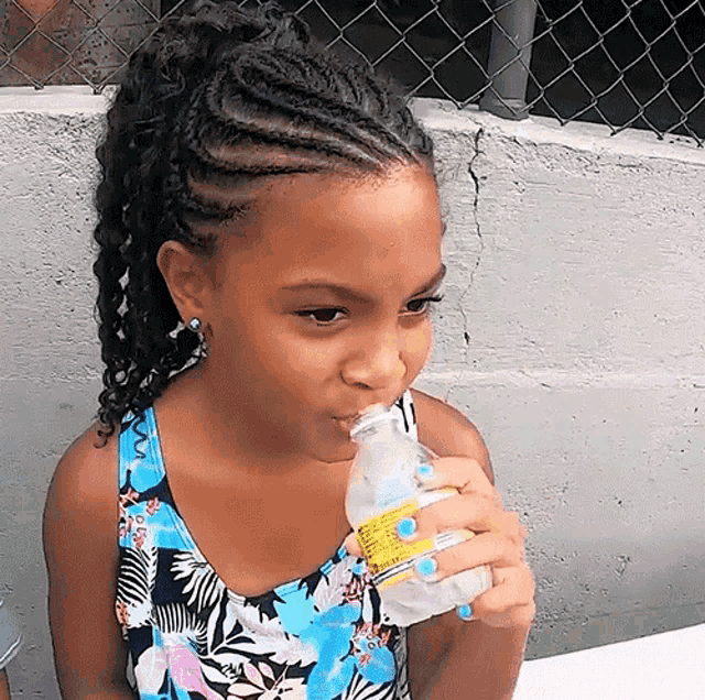 a little girl is drinking water from a bottle with a label that says ' tropicana ' on it