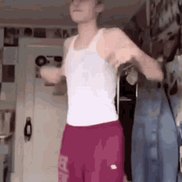 a young man in a white tank top and pink shorts is dancing .