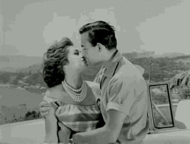 a man and a woman kissing in front of a body of water