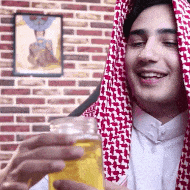 a man wearing a red and white scarf holds a glass of beer in front of a brick wall