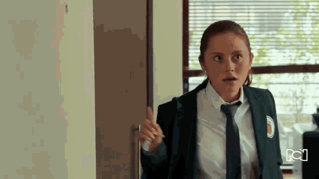 a girl in a school uniform is standing in front of a door with the letter n on it