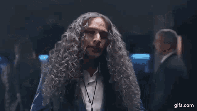 a man in a blue suit and white shirt with long hair is dancing .