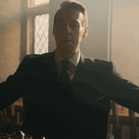 a man in a suit and tie sits at a table with his arms outstretched