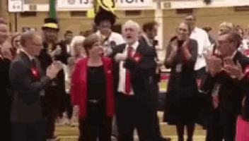 a man in a suit and tie is standing in front of a crowd of people clapping .