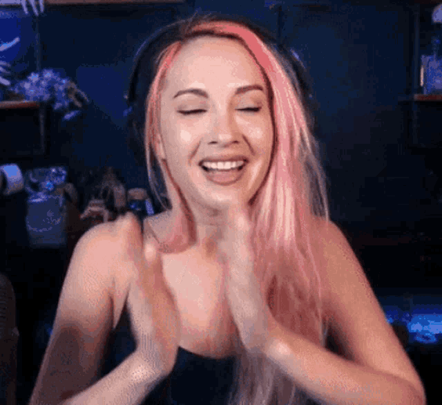 a woman with pink hair is smiling and clapping her hands .