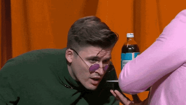 a man wearing sunglasses is talking to a woman in a pink sweater